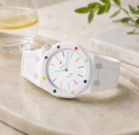 White watch with colorful hour markers on marble surface next to glass of water and green plant