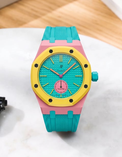 Colorful watch with turquoise band, pink case, yellow bezel, and turquoise dial on white surface